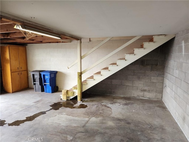 unfinished basement featuring concrete block wall and stairs