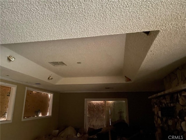 room details featuring visible vents, a raised ceiling, and a textured ceiling