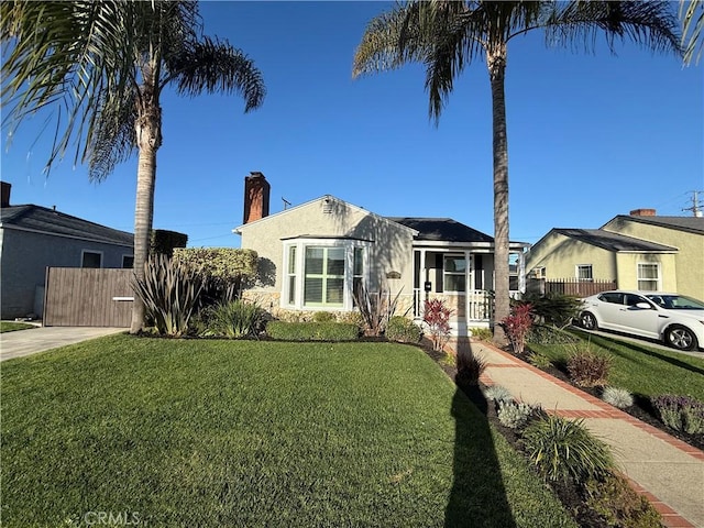 view of front of home with stucco siding, a chimney, fence, and a front yard