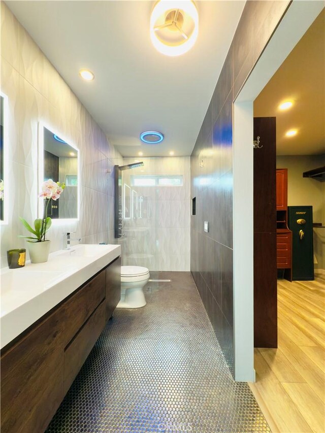 full bathroom with tile patterned flooring, toilet, vanity, tile walls, and a tile shower