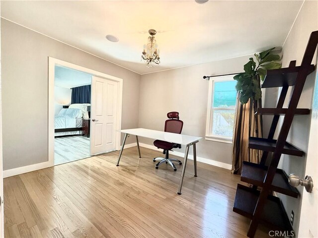 office with light wood-type flooring, baseboards, and an inviting chandelier