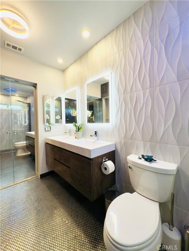 bathroom with visible vents, toilet, tile patterned flooring, an enclosed shower, and tile walls