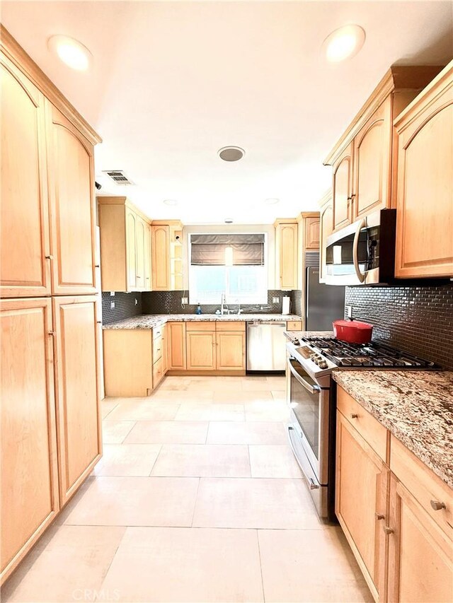 kitchen with stainless steel appliances, a sink, backsplash, and light brown cabinetry