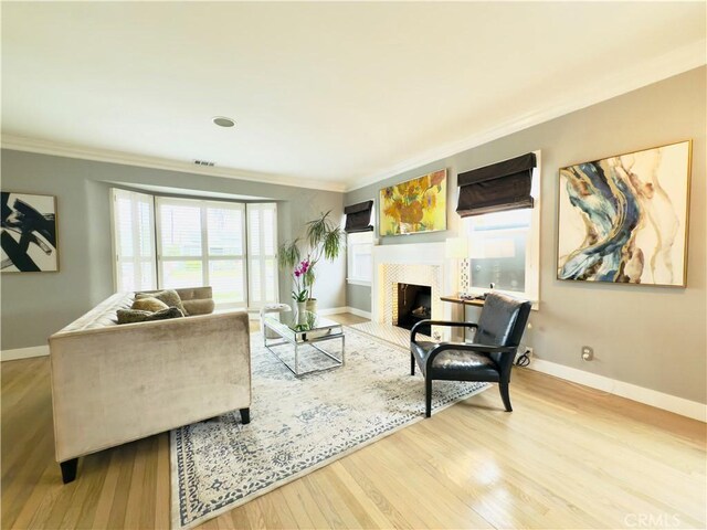 living room with a fireplace with flush hearth, ornamental molding, baseboards, and wood finished floors