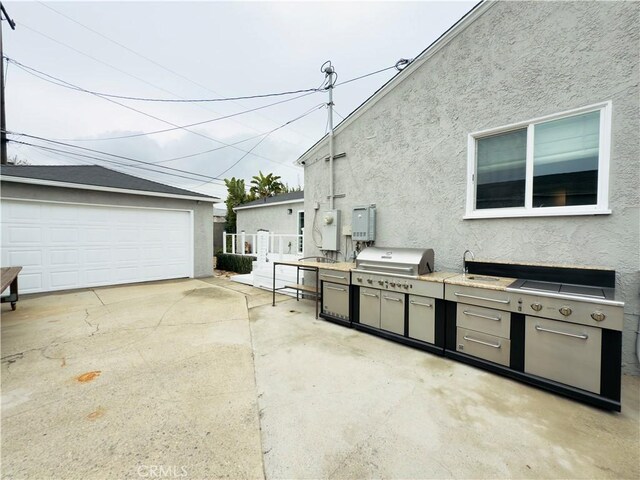 view of patio / terrace featuring a garage, grilling area, exterior kitchen, and an outdoor structure