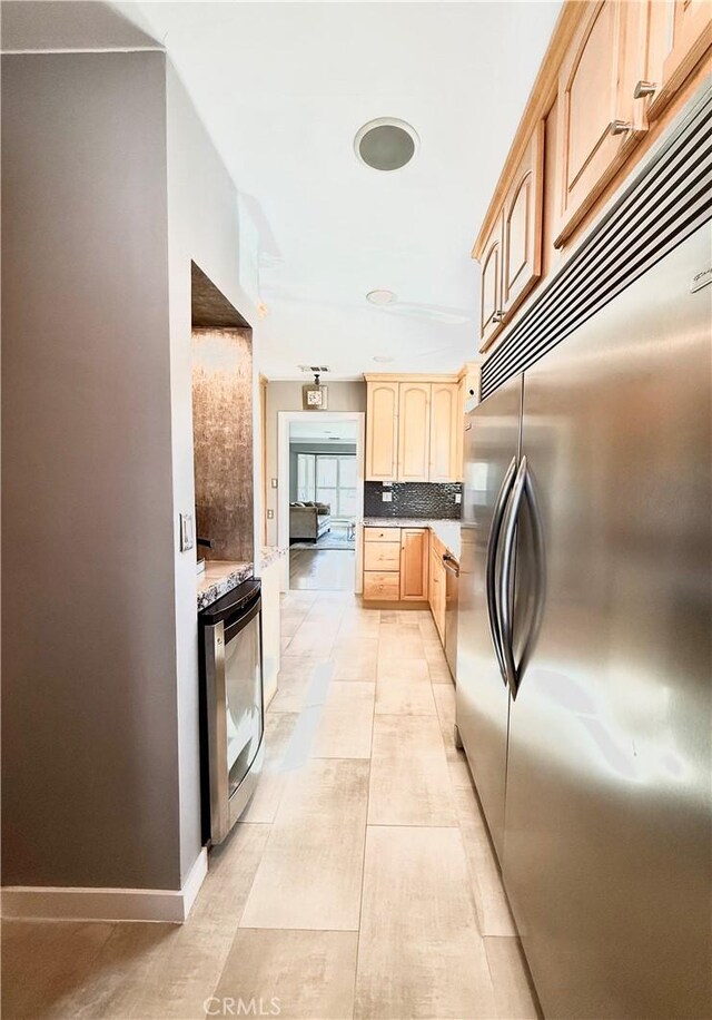 kitchen with light tile patterned floors, light brown cabinets, built in refrigerator, baseboards, and tasteful backsplash