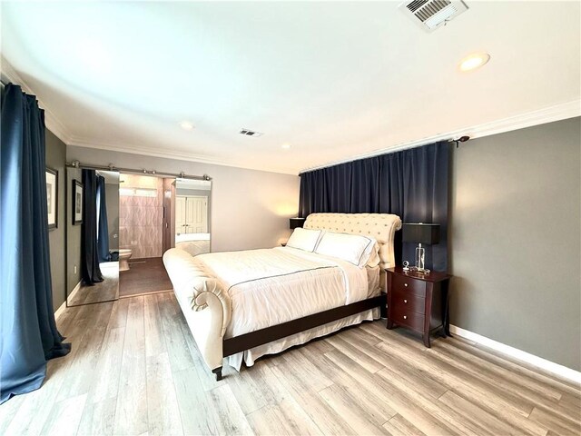 bedroom featuring light wood finished floors, a barn door, visible vents, and crown molding