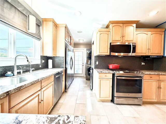 kitchen featuring a sink, appliances with stainless steel finishes, light brown cabinets, and stacked washer and clothes dryer