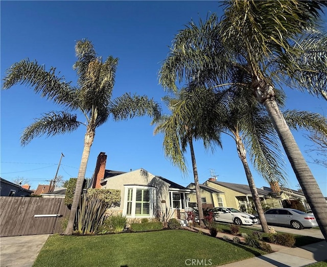 view of front facade with stucco siding, a chimney, fence, and a front yard