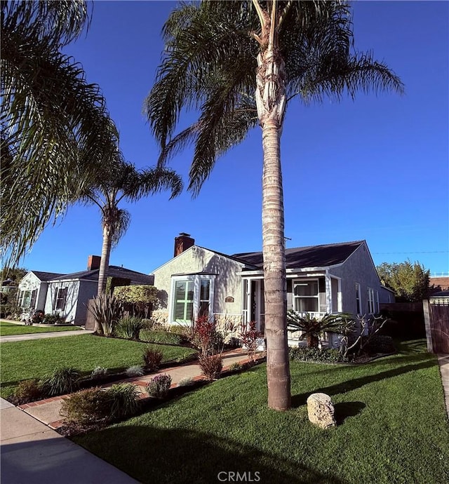 view of front of property with a chimney, a front yard, and stucco siding