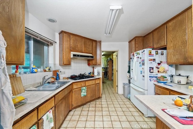 kitchen featuring freestanding refrigerator, brown cabinets, a sink, and under cabinet range hood