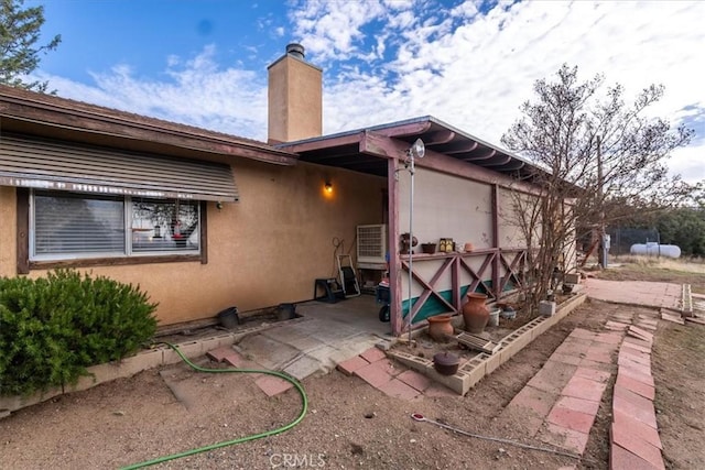 rear view of property with a patio area, a chimney, and stucco siding