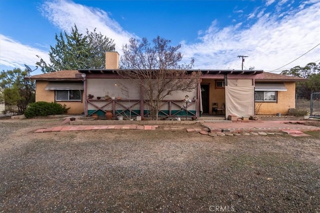 rear view of house featuring a chimney and stucco siding