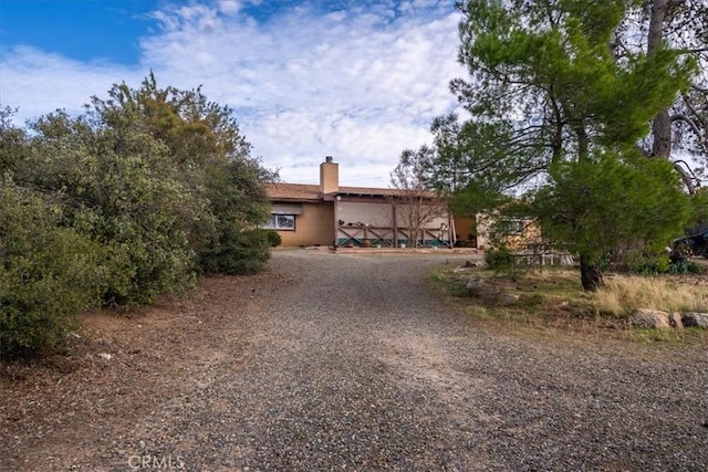 view of front facade featuring gravel driveway, a chimney, and stucco siding