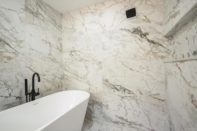 bathroom featuring stone wall and a freestanding tub