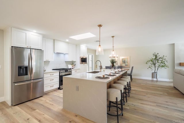 kitchen with a skylight, a breakfast bar, stainless steel appliances, light wood-style floors, and a sink