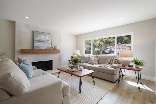 living room with recessed lighting, a fireplace with raised hearth, light wood-style flooring, and baseboards