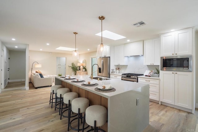 kitchen with a breakfast bar, custom exhaust hood, visible vents, appliances with stainless steel finishes, and a sink