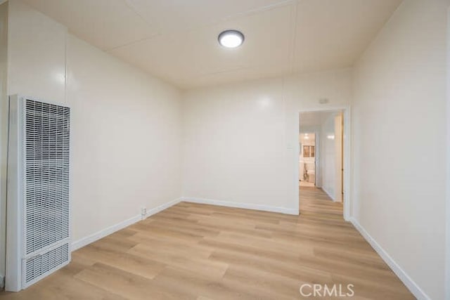 spare room featuring light wood-style flooring, baseboards, and a heating unit