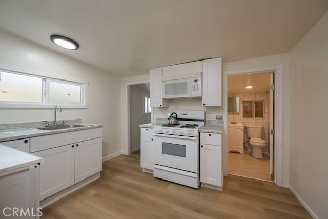 kitchen with light wood finished floors, light countertops, white cabinets, white appliances, and a sink