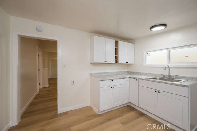 kitchen with white cabinetry, open shelves, light countertops, and a sink