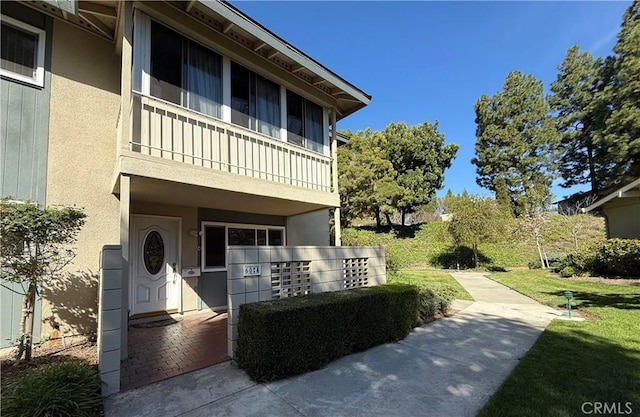 view of front of home featuring a front yard, a balcony, and stucco siding