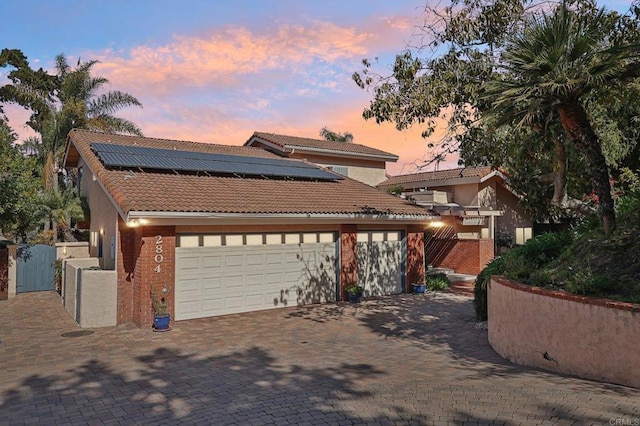 view of front of house featuring solar panels, brick siding, a tile roof, decorative driveway, and a gate