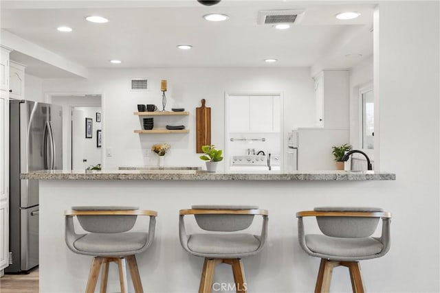 kitchen with freestanding refrigerator, visible vents, a kitchen bar, and white cabinetry