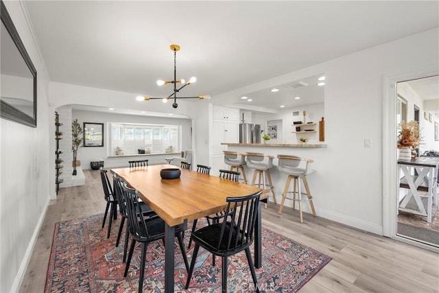 dining room featuring arched walkways, a notable chandelier, recessed lighting, light wood-style floors, and baseboards