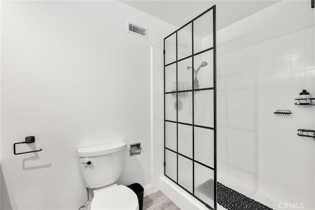 full bathroom featuring toilet, a tile shower, visible vents, and baseboards