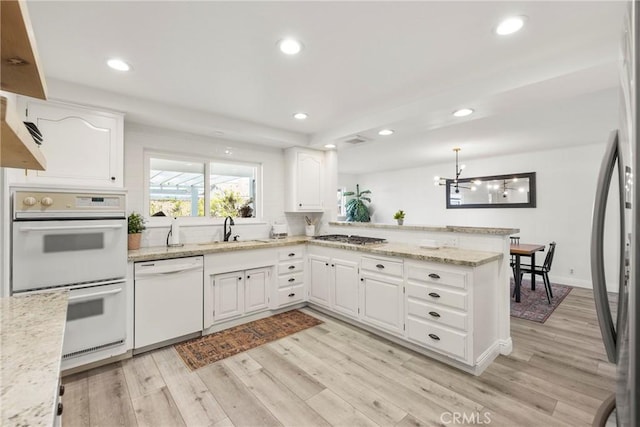 kitchen featuring light wood finished floors, white cabinets, appliances with stainless steel finishes, a peninsula, and a sink