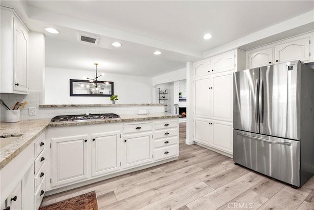 kitchen featuring tasteful backsplash, light wood-style flooring, appliances with stainless steel finishes, white cabinets, and a peninsula