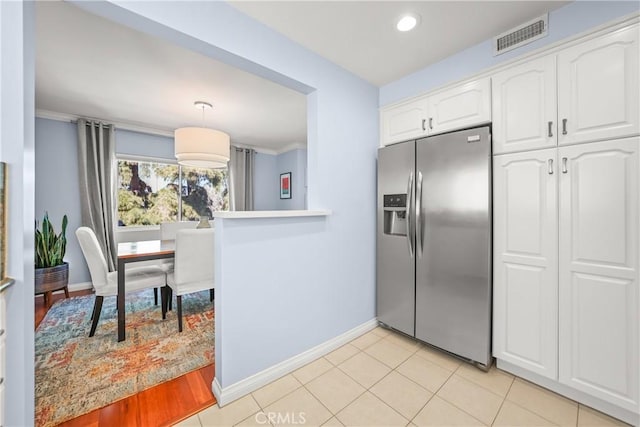 kitchen with light tile patterned floors, visible vents, ornamental molding, white cabinetry, and stainless steel fridge with ice dispenser