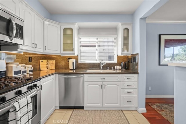 kitchen with light tile patterned flooring, a sink, white cabinets, appliances with stainless steel finishes, and dark countertops