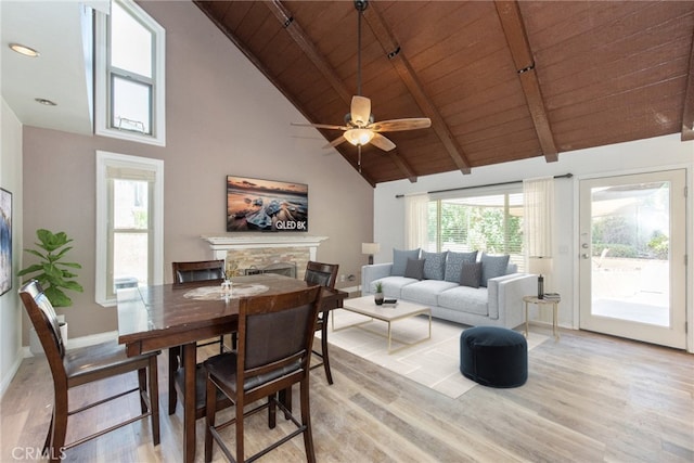 dining space with wooden ceiling, a stone fireplace, light wood-type flooring, high vaulted ceiling, and beam ceiling