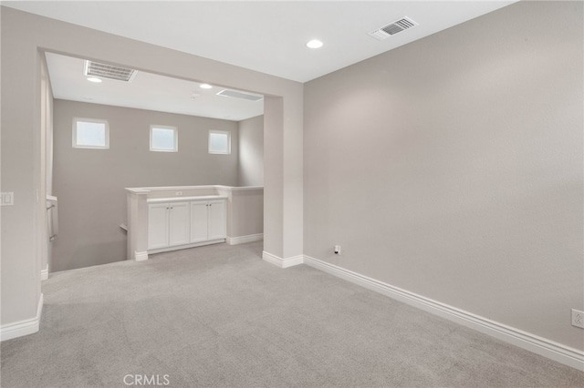 below grade area with light carpet, visible vents, and baseboards