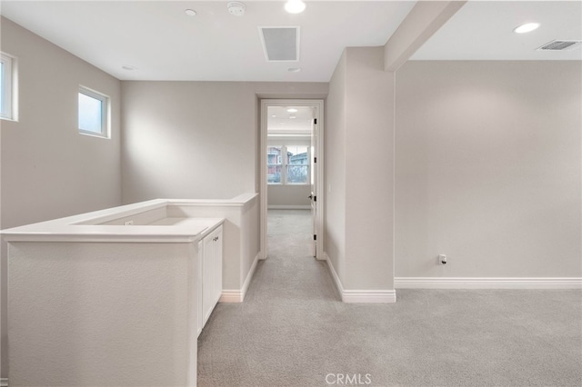 hallway with light carpet, a wealth of natural light, and visible vents