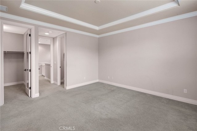 unfurnished bedroom with carpet floors, ornamental molding, a walk in closet, and a tray ceiling