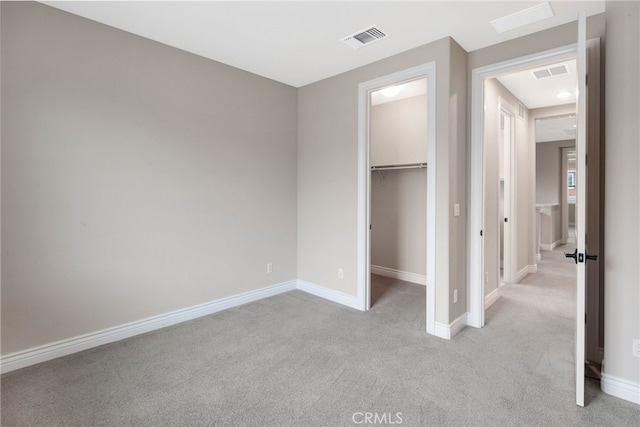 unfurnished bedroom featuring baseboards, visible vents, a walk in closet, and light colored carpet