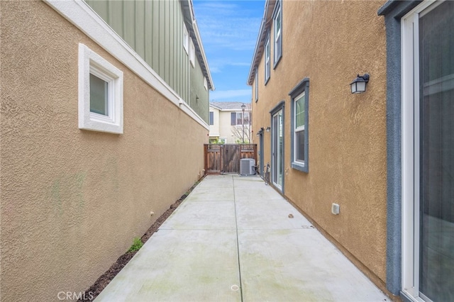 view of side of home with central AC unit, a patio area, fence, and stucco siding