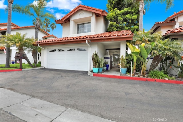 mediterranean / spanish-style house with a garage, stucco siding, driveway, and a tiled roof