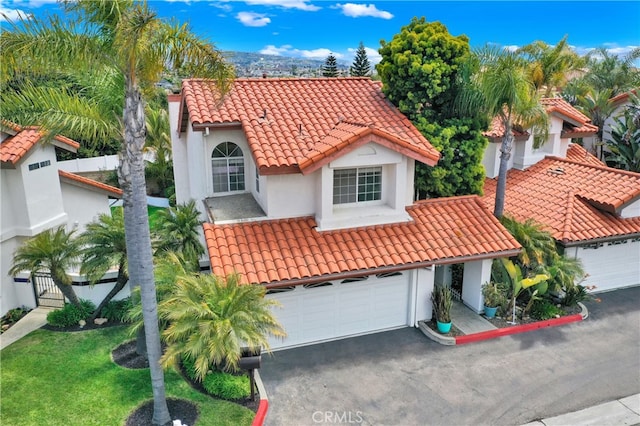 mediterranean / spanish house with fence, aphalt driveway, stucco siding, and a tiled roof