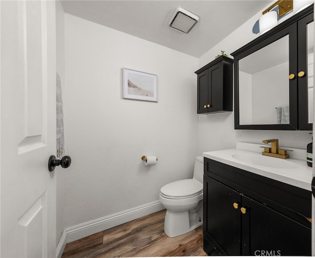 half bath with toilet, baseboards, wood finished floors, and vanity