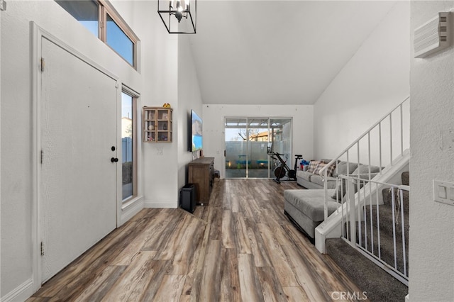 foyer featuring stairs, a wall unit AC, wood finished floors, and a towering ceiling