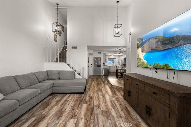 living room with stairs, wood finished floors, a towering ceiling, and an inviting chandelier