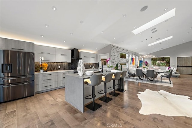 kitchen with light wood finished floors, stainless steel fridge, an island with sink, modern cabinets, and a breakfast bar area