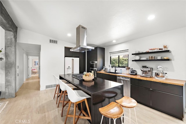 kitchen with island exhaust hood, visible vents, stainless steel appliances, and a sink