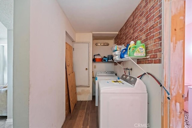 clothes washing area with wood finished floors, brick wall, and washing machine and clothes dryer