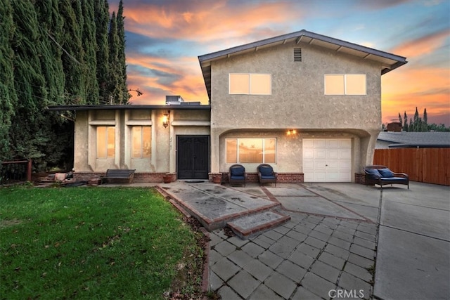 rear view of house with stucco siding, driveway, a yard, and fence