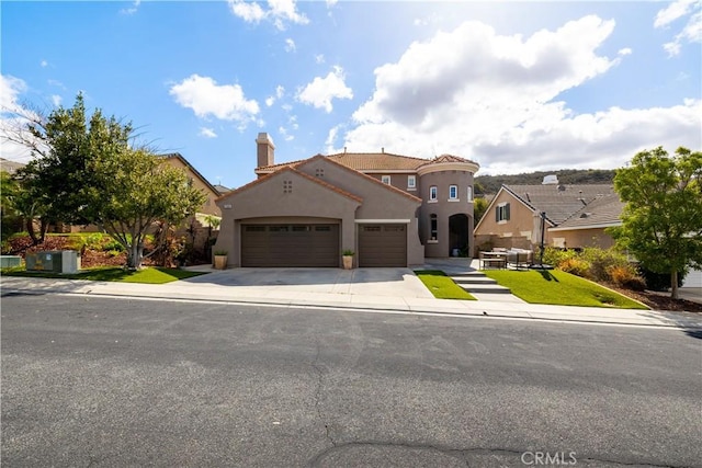 mediterranean / spanish house with driveway, a chimney, an attached garage, and stucco siding